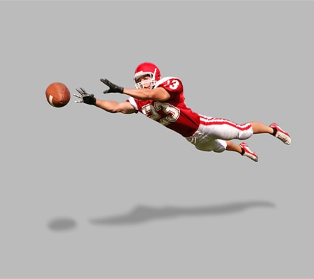 Football receiver is horizontal in the air, leaping to catch football