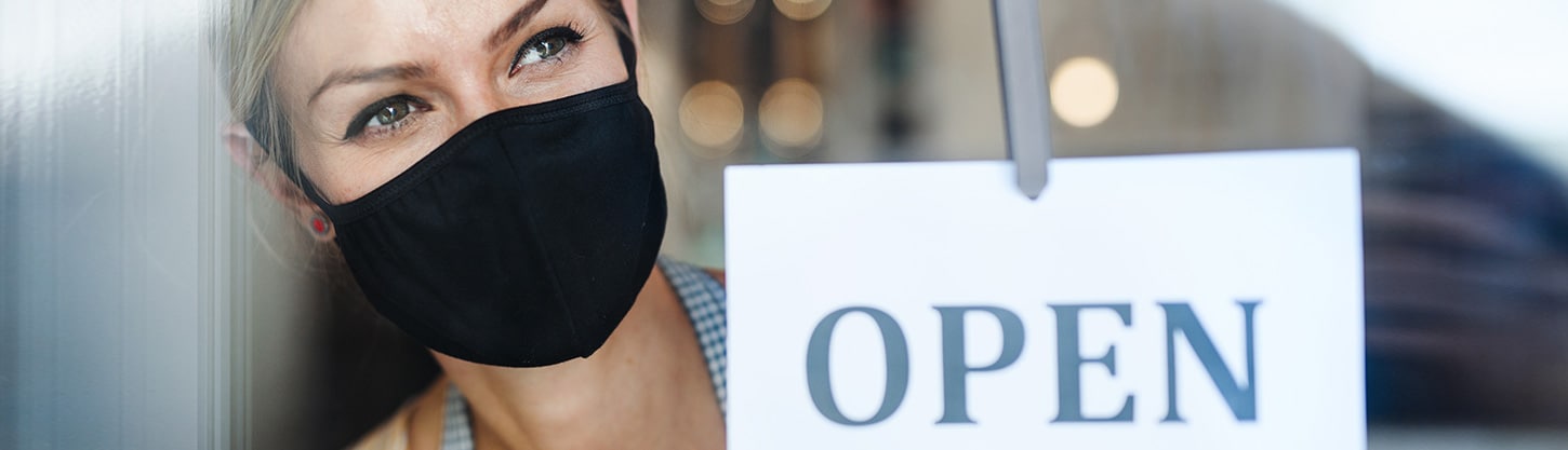 Woman wearing face mask putting up "open" sign on door.